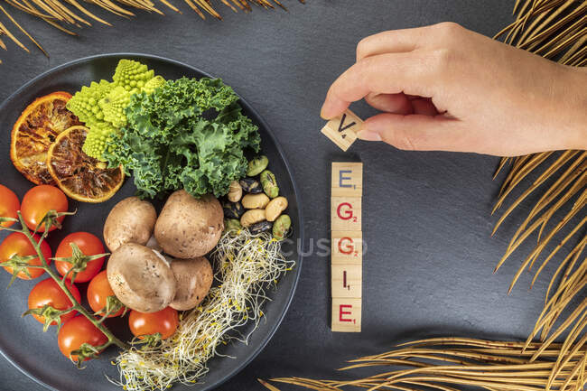 Top view of anonymous cook compiling decorative title near assorted vegetables and fruits with nuts on plate on gray background — Stock Photo