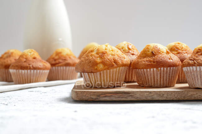 Leckere hausgemachte frisch gebackene süße Muffins in Pappbechern auf dem Tisch mit Glas mit frischer Milch arrangiert — Stockfoto