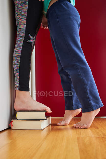 Side view of crop unrecognizable kids standing on pile of books near wall and measuring their height — Stock Photo