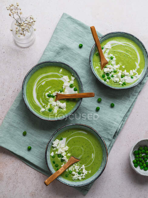 Top view of delicious pea cream soup in bowls served on table with napkin and vase with flowers — Stock Photo