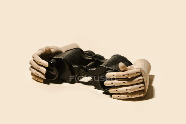 Decorative flexible wooden hands placed with retro binoculars on beige background in light studio — Stock Photo