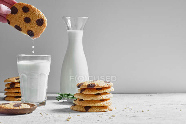 Cultiver une personne anonyme trempant de délicieux biscuits maison sucrés avec des pépites de chocolat dans un verre de lait frais — Photo de stock