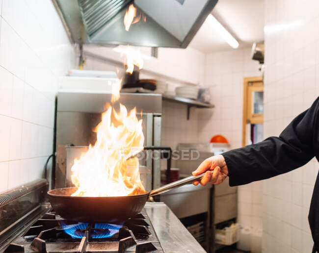 Вид збоку врожаю безликий кухар готує страву на сковороді на плиті під час роботи на кухні ресторану — стокове фото
