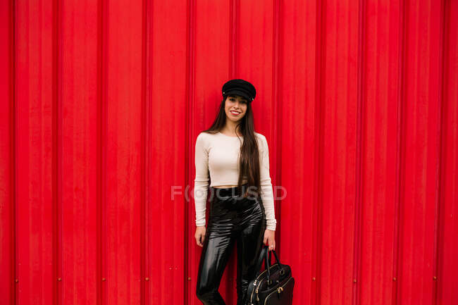 Empresária feliz vestindo roupas da moda em pé na rua no fundo da parede vermelha e olhando para a câmera — Fotografia de Stock