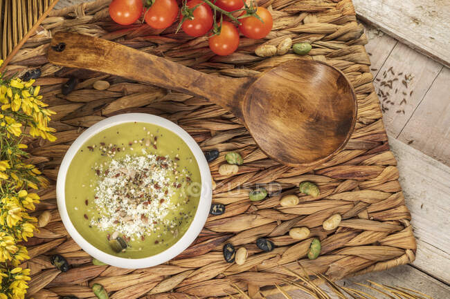 Vista dall'alto di appetitosa zuppa di crema vegana con pistacchi schiacciati in cima su stuoia di vimini con cucchiaio di legno — Foto stock