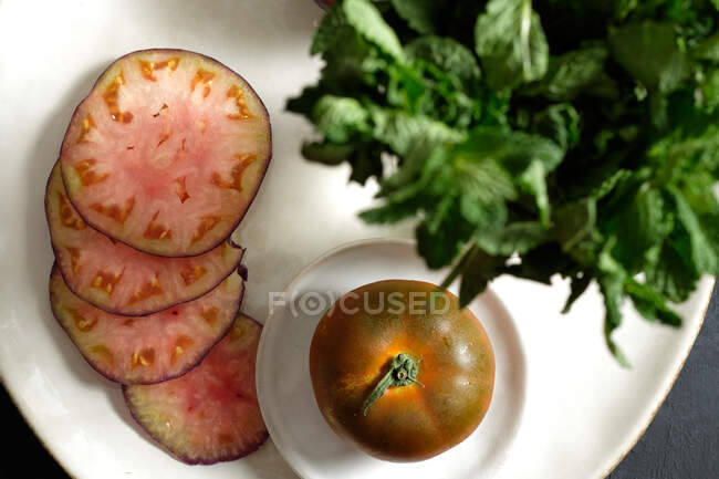 Top view of fresh whole and sliced black tomatoes on table and green mint during healthy meal preparation — Stock Photo