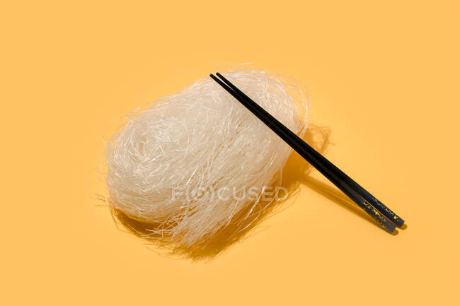 Porzione di tagliatelle di riso con bacchetta nera appoggiata su superficie chiara su fondo giallo in studio — Foto stock