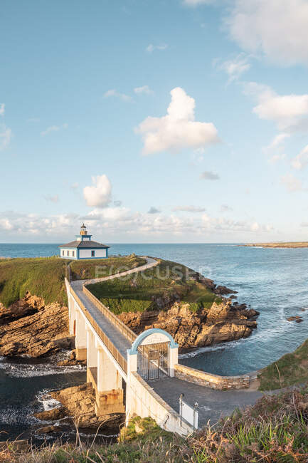 Spectacular scenery of bridge leading to rocky island covered with green grass with lighthouse placed in wavy ocean in Faro Illa Pancha in Galicia in Spain in daytime — Stock Photo