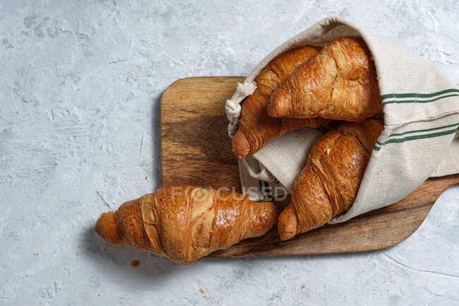 Croissants recién horneados servidos en tabla de cortar de madera con servilleta en la mesa para el desayuno - foto de stock