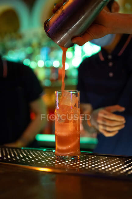 Detalle de la mano del camarero irreconocible trabajando en el bar con su agitador y vertiendo un cóctel en el vaso - foto de stock