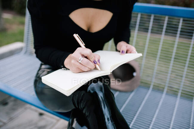 Високий кут урожаю нерозпізнаної жінки-підприємця сидить на лавці в місті і пише бізнес-план в записнику — стокове фото