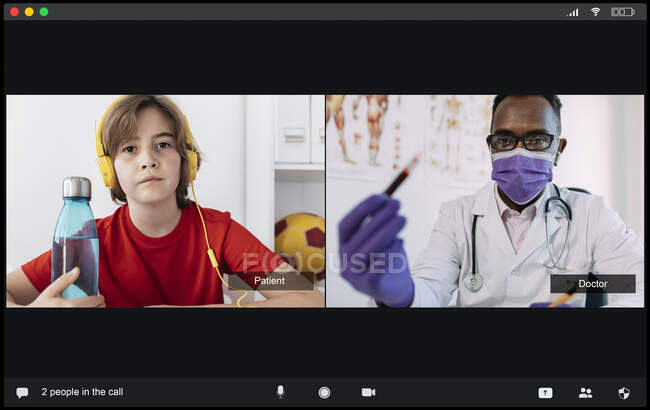 Концентрований молодий чорношкірий лікар у медичній формі та маска, що показує пробірку з аналізом крові до уважного пацієнта хлопчика під час відеодзвінка — стокове фото