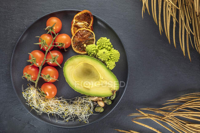 Top view of fresh half of avocado near bunch of cherry tomatoes and sprouts with Romanesco broccoli and nuts on plate — Stock Photo