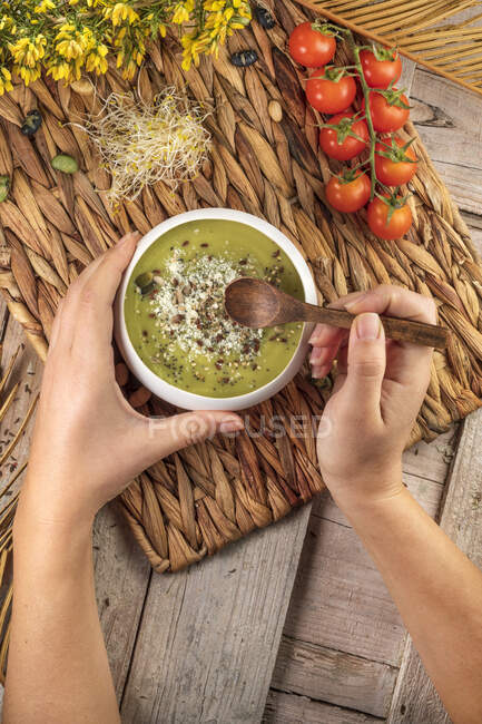Top view of crop unrecognizable cook with wooden spoon and bowl of appetizing cream soup with crushed pistachios and spices — Stock Photo