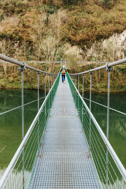 Back view of elderly female hiker in casual clothes strolling on suspension bridge in daytime — Stock Photo