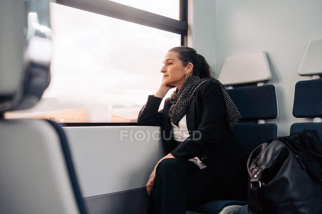 Side view of middle aged female with closed eyes leaning on hand while sitting on passenger seat during ride in wagon looking outside through the windows — Stock Photo