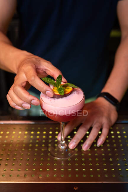 Mains de barman méconnaissable décorer un cocktail avec des feuilles de menthe et des fruits de la passion dans le bar — Photo de stock