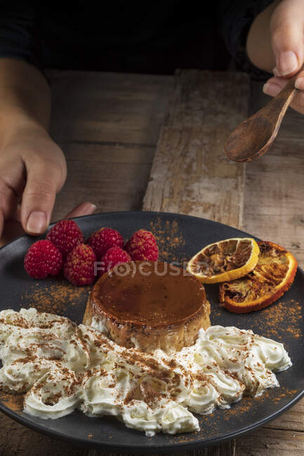 From above of crop anonymous cook with plate of yummy baked flan with ripe raspberries and cinnamon powder — Stock Photo