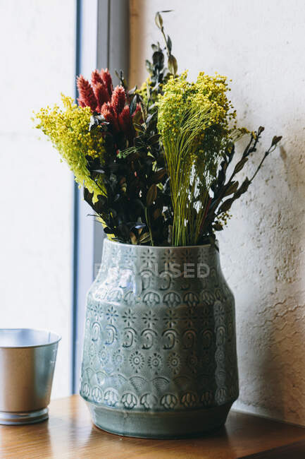 Verschiedene bunte blühende Blumen in Keramikvase auf hölzerner Fensterbank neben dem Fenster platziert — Stockfoto