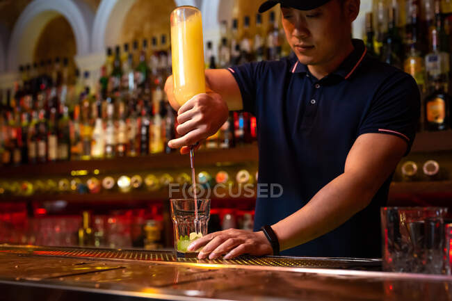 Jeune barman asiatique versant du jus de citron dans le verre tout en préparant un cocktail mojito au bar — Photo de stock