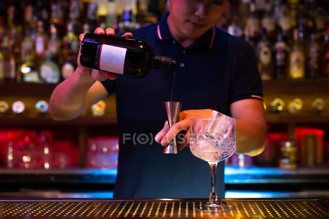 Joven camarero asiático vertiendo ginebra en jigger mientras prepara un cóctel gin tonic en el bar - foto de stock