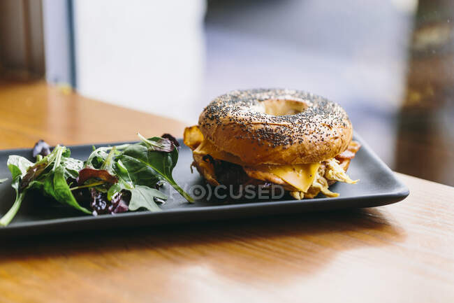 Аппетитный бутерброд с сыром и курицей на тарелке с салатом из руколы на столе в кафе — стоковое фото