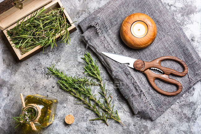 Top view of rosemary sprigs with green leaves in small chest near glass bottle with oil and scissors near candle in candlestick on textile on table — Stock Photo