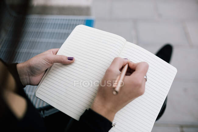 Alto angolo di coltura irriconoscibile imprenditore femminile seduto sulla panchina in città e la scrittura di business plan in notebook — Foto stock