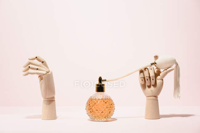 Stylish transparent bottle of perfume placed between wooden hands placed on pink background in light studio — Stock Photo
