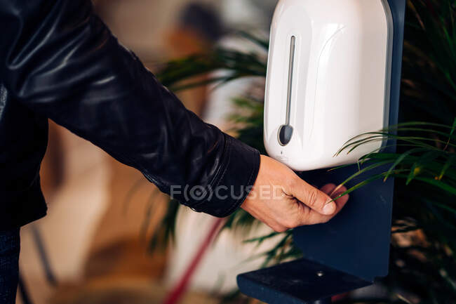 Crop anonymous male in leather jacket using gel dispenser during coronavirus period in building — Stock Photo