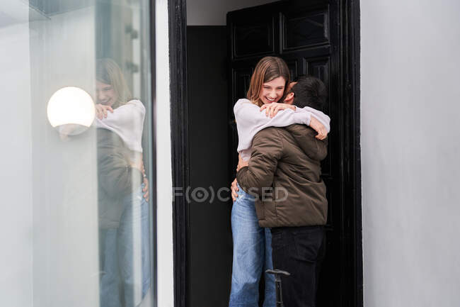 Joyeux jeune femme rencontre petit ami anonyme avec des bagages retournés du voyage d'affaires sur le seuil de la maison tout en étreignant — Photo de stock