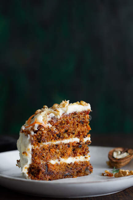 Yummy cake with cream cheese served on plate with fresh carrot slices and walnuts — Stock Photo