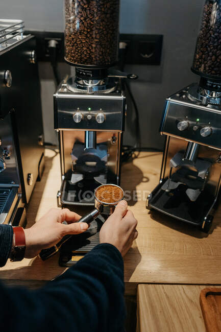From above crop unrecognizable barista using coffee grinder while preparing aromatic fresh coffee in cafe in daytime — Stock Photo