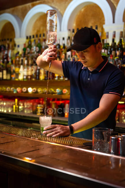 Joven camarero asiático vertiendo ron en el vaso mientras prepara cóctel mojito en el bar - foto de stock