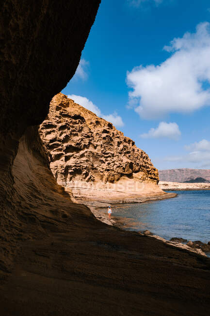 Voyageuse marchant sur le rivage avec des falaises rocheuses près de la mer ondulante pendant les vacances dans un pays exotique ensoleillé — Photo de stock