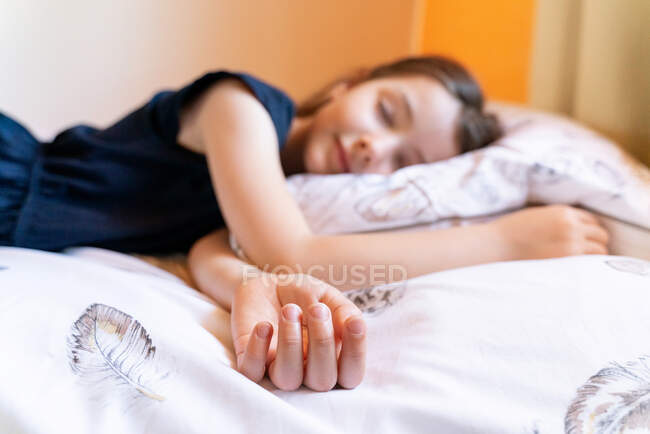 Petite fille mignonne en vêtements de nuit sombres dormant paisiblement sur un lit doux dans la chambre du matin claire — Photo de stock