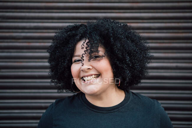 Content adult overweight female curly hair against ribbed wall in daytime and looking at camera — Stock Photo