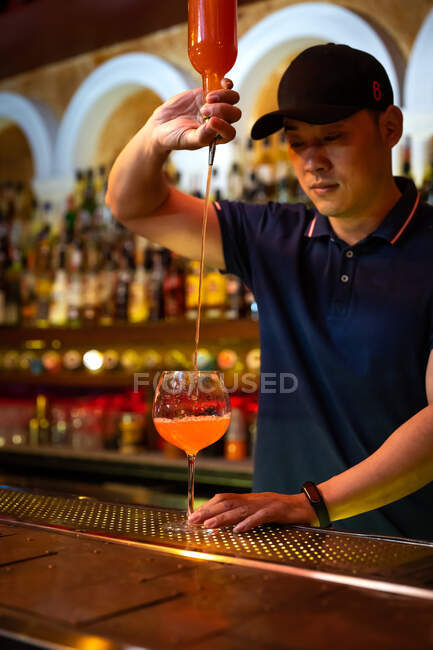 Jovem barman asiático derramando suco de toranja no copo enquanto prepara um coquetel no bar — Fotografia de Stock