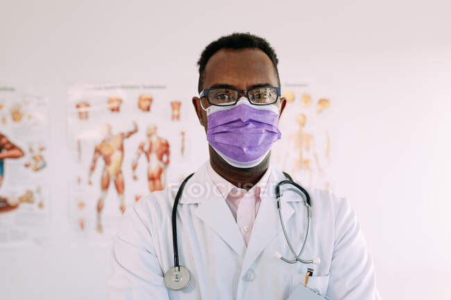 Médico profissional afro-americano com estetoscópio em uniforme e óculos olhando para a câmera no hospital — Fotografia de Stock