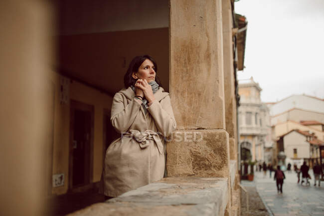 Jeune femme timide en vêtements d'extérieur touche ses mains tout en regardant loin dans la construction âgée en plein jour — Photo de stock