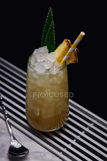 From above table with glass of yellow cocktail with ice cubes and refreshing cocktail garnished with spiky leaves and striped straw — Stock Photo