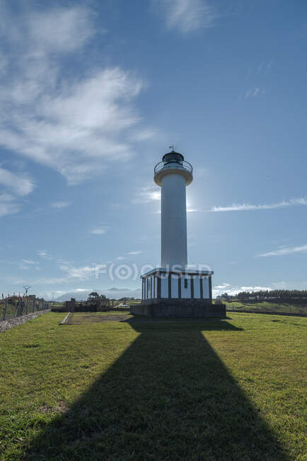 Ombre menant au phare blanc placé à Faro de Lastres dans les Asturies en Espagne sous un ciel bleu sans nuages en journée — Photo de stock