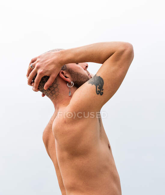 Вид збоку спокійного чоловіка з татуйованою лисицею, що стоїть з закритими очима в природі проти річки та гори в похмурий день — стокове фото