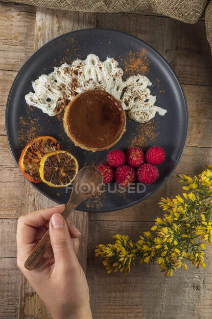 Сверху кукурузы анонимный повар с тарелкой вкусного запеченного пирога с спелыми малинами и порошком корицы — стоковое фото