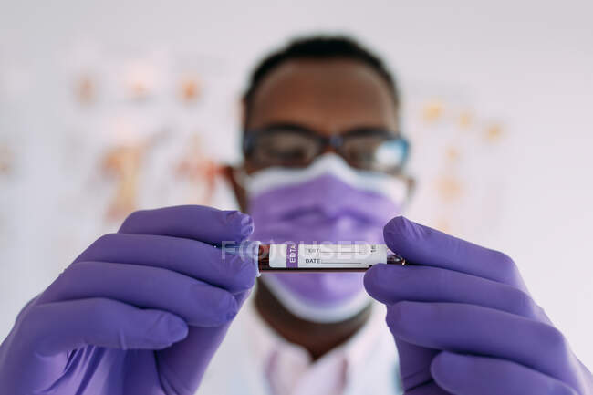 African American male doctor in medical glove demonstrating test tube with blood sample on white background — Stock Photo
