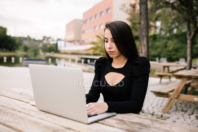 Сосредоточенная женщина-предприниматель сидит за столом с ноутбуком в парке и работает удаленно — стоковое фото