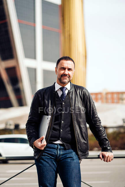 Empreendedor masculino de meia-idade confiante em roupas elegantes com netbook olhando para a câmera na cidade — Fotografia de Stock