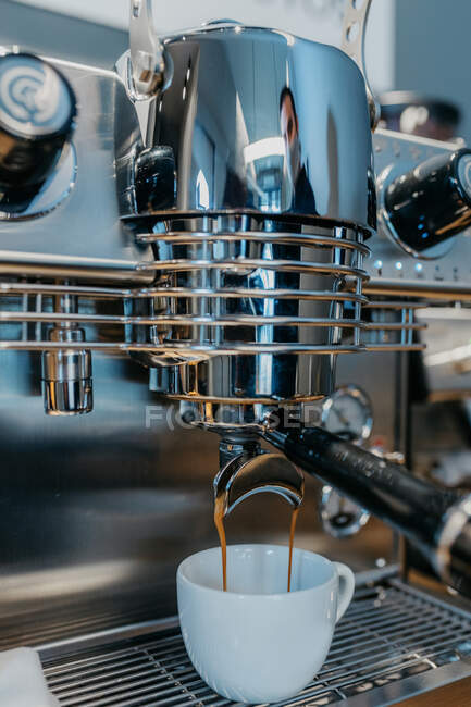 Machine à café professionnelle moderne versant du café chaud frais dans une tasse blanche dans un café pendant la journée — Photo de stock