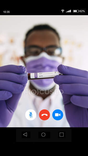 Anonyme médecin afro-américain professionnel dans des gants médicaux démontrant le vaccin en ligne en appel vidéo en soft focus — Photo de stock