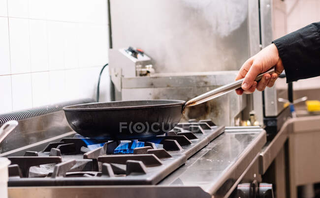 Side view of crop unrecognizable cook preparing dish in frying pan on stove in kitchen of restaurant — Stock Photo